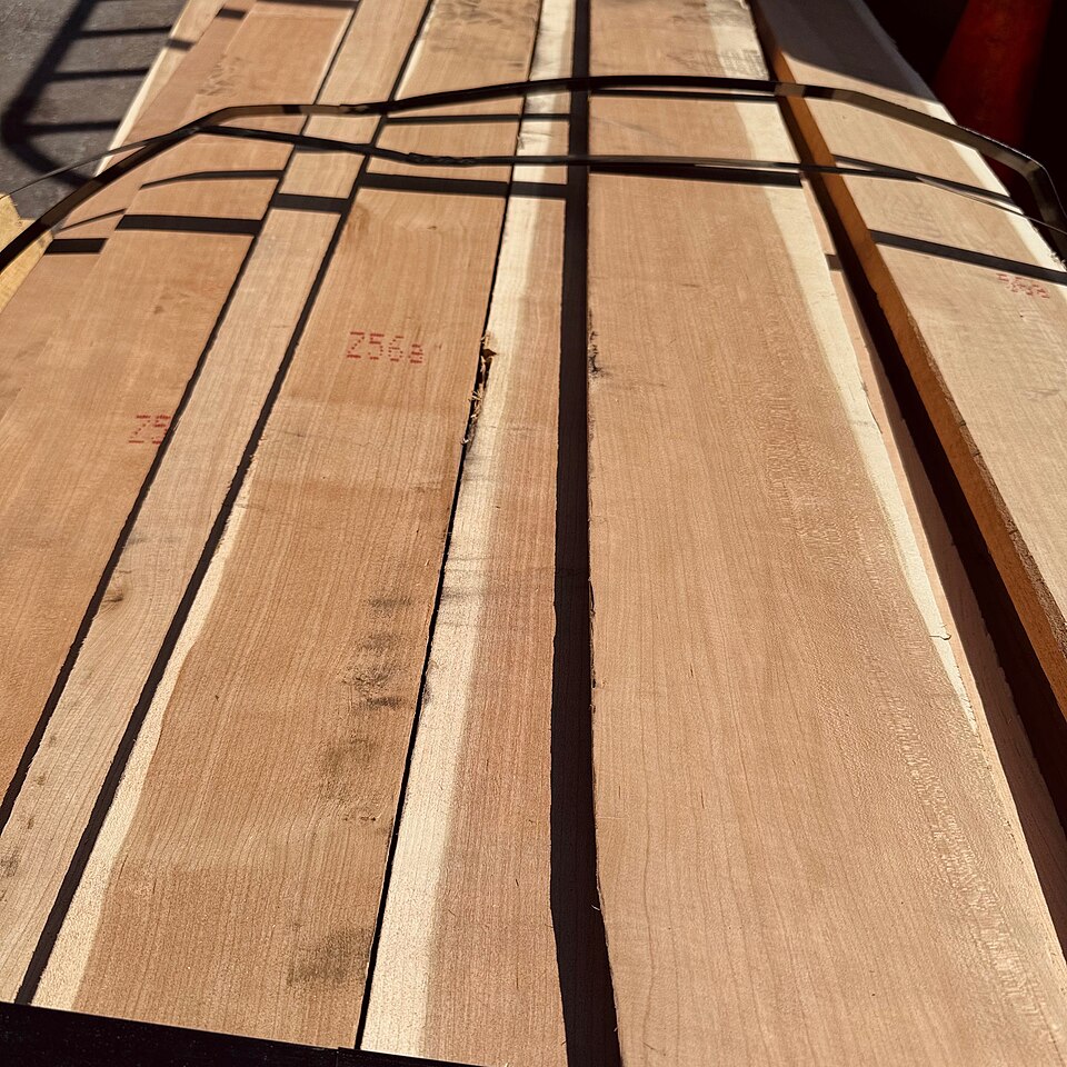 A banded stack of freshly milled quartersawn cherry boards at a lumberyard, pale salmon-pink with straight vertical grain