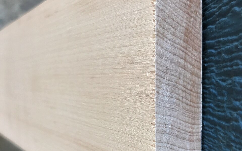 A planed hard maple board, pale cream face grain running to a quartersawn edge with a band of subtle curl figure