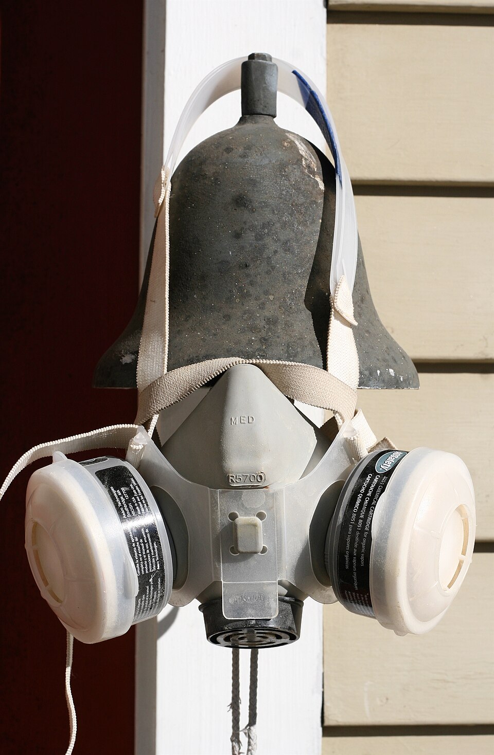 A well-used gray half-mask respirator hanging on a wall, fitted with two organic-vapor cartridges labeled for organic vapors